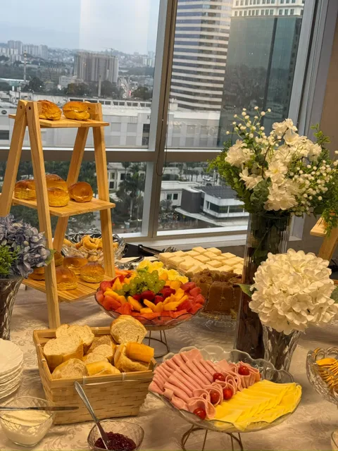 Mesa de coffee break com frios e pães diante de janelas